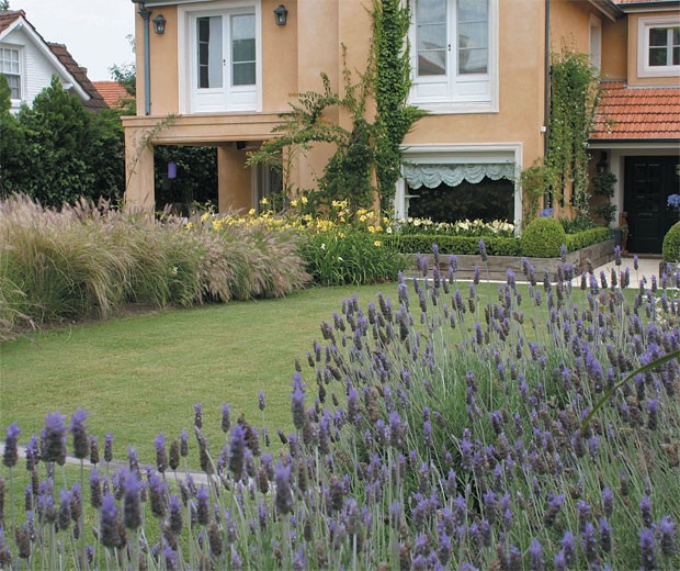 La fachada de la casa vestida por las plantas dentro de los contenedores de quebracho, y el paño central de césped de Bermuda tifton en dos niveles